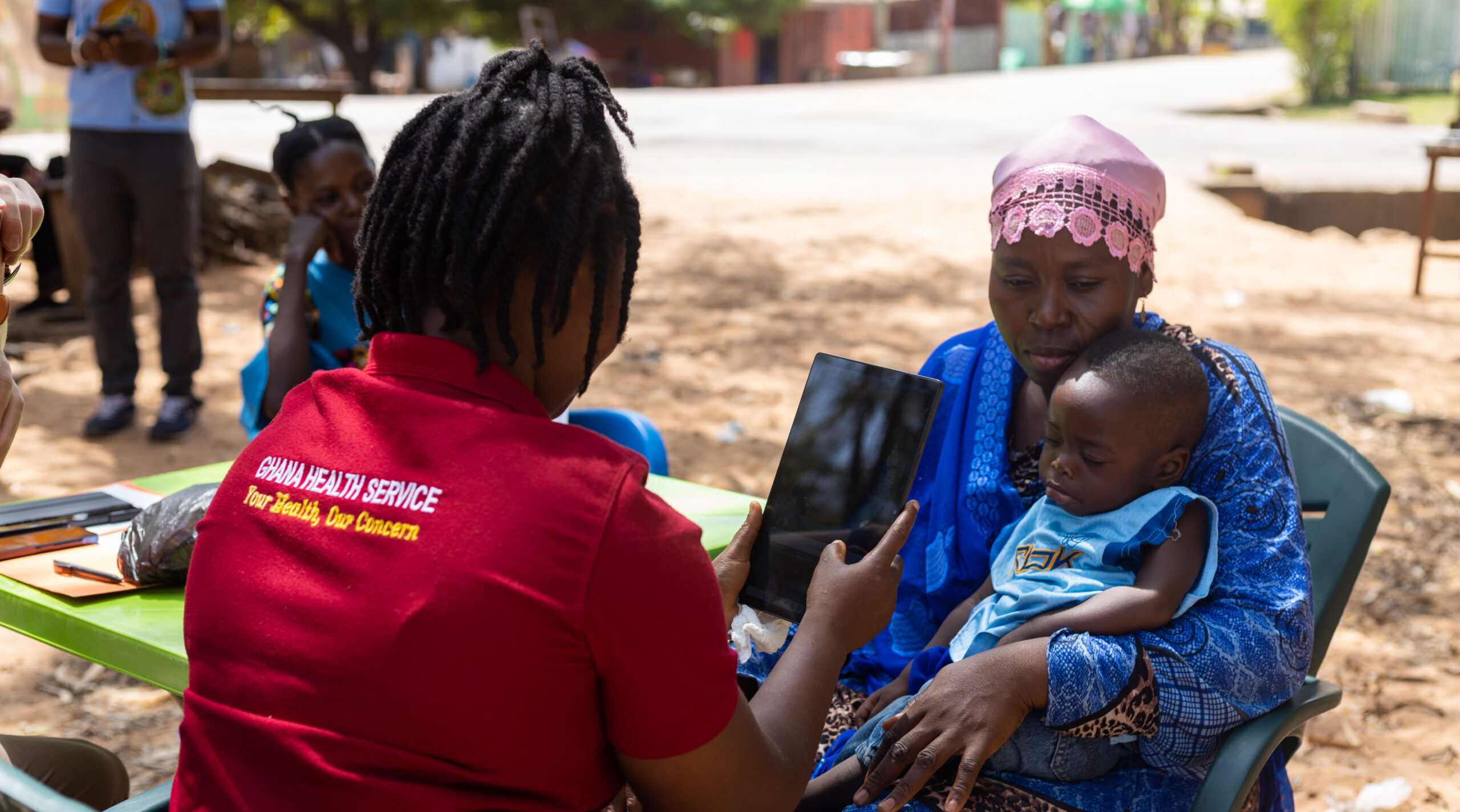 Ghana Health Service Health Worker uses Simprints' app on a tablet to scan biometrics of a baby in a rural setting